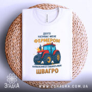 Футболка фермер швагро, біла, зображена зверху, на плетеній кошику, принт з червоним трактором та жовтим текстом.