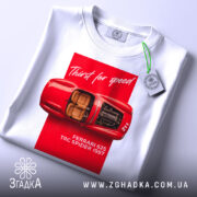 Футболка Ferrari білого кольору, зображена зверху, фон світлий, принт з червоним автомобілем Ferrari 625 TRC Spider 1957, текст 'Thirst for speed' на червоному фоні, на футболці є етикетка з зеленим шнурком.