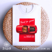 Футболка Ferrari білого кольору, зображена зверху на плетеному кошику, фон світлий, принт з червоним автомобілем Ferrari 625 TRC Spider 1957, текст 'Thirst for speed' на червоному фоні.