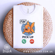 Футболка fih is calling. Біла футболка, складена на плетеній основі, фон світлий, принт чіткий, рибка оранжевого кольору з великими очима, текст 'FiH' та 'PICK UP' під рибкою.