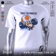 Футболка фітнес настрій, біла, зображена на манекені, фон світло-сірий, принт з персонажем, що піднімає штангу, текст 'TRUST THE PROCESS' над ним.