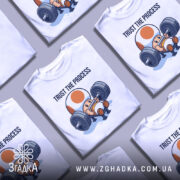 Футболка фітнес настрій, біла, зображена на манекені, фон світло-сірий, принт з персонажем, що піднімає штангу, текст 'TRUST THE PROCESS' над ним.