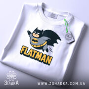 Футболка флетмен білого кольору, складена на поверхні, з видимим ярликом, фон світло-сірий, принт з персонажем у костюмі Бетмена, що летить, з написом 'FLATMAN' під ним.