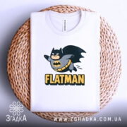 Футболка флетмен білого кольору, складена на плетеній кошику, фон світло-сірий, принт з персонажем у костюмі Бетмена, що летить, з написом 'FLATMAN' під ним.
