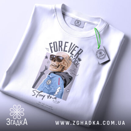 Футболка forever cool, білого кольору, складена на столі, фон світло-сірий, принт з черепом у сонцезахисних окулярах та синій куртці, на комірці видна етикетка.