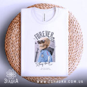 Футболка forever cool, білого кольору, складена на плетеній основі, фон світло-сірий, принт з черепом у сонцезахисних окулярах та синій куртці, текст 'Stay true' під малюнком.