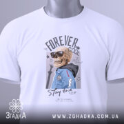Футболка forever cool, білого кольору, складена на столі, фон світло-сірий, принт з черепом у сонцезахисних окулярах та синій куртці, на комірці видна етикетка.