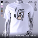 Футболка фото на паспорт: біла футболка на манекені, з принтом, що містить малюнок усміхненої людини з довгим волоссям, яка показує знак миру, текст "МОЄ ФОТО НА ПАСПОРТ:" розташований зверху, фон світло-сірий.