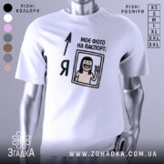 Футболка фото на паспорт: біла футболка на манекені, з принтом, що містить малюнок усміхненої людини з довгим волоссям, яка показує знак миру, текст "МОЄ ФОТО НА ПАСПОРТ:" розташований зверху, фон світло-сірий.