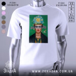 Футболка Фріда білого кольору, зображена на манекені, фон сірий, принт з портретом жінки з яскравим головним убором та зеленим фоном.