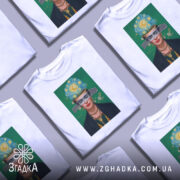 Футболка Фріда білого кольору, зображена на манекені, фон сірий, принт з портретом жінки з яскравим головним убором та зеленим фоном.