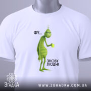 Футболка фу люди. Біла футболка, складена на поверхні, з принтом зеленого персонажа, що тримає чашку. Фон світлий, ракурс зверху, видно етикетку з логотипом, текст на принті: 'ФУ... ЗНОВУ ЛЮДИ!'