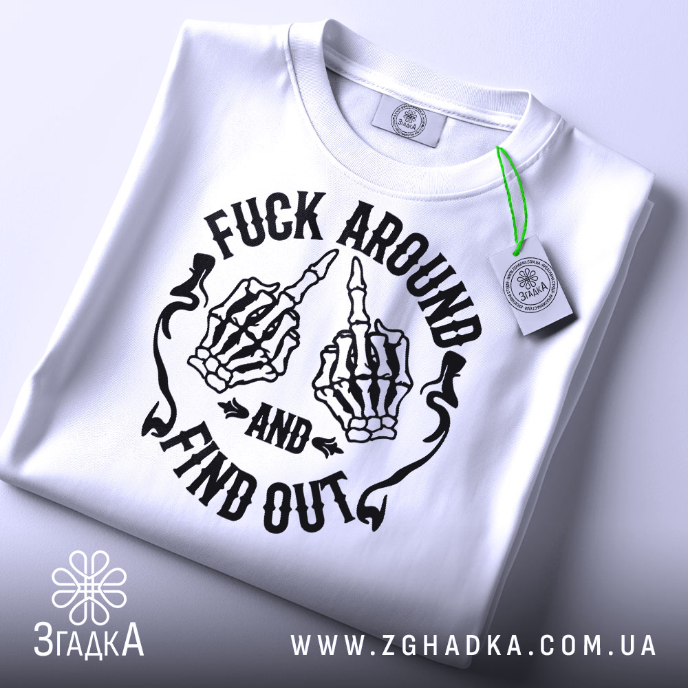Футболка fuck around find out, білого кольору, складена на поверхні, з верхнього ракурсу, фон світло-сірий, принт з чорними скелетними руками, що показують середній палець, з написом 'AND' та 'FIND OUT', на етикетці зелена стрічка.