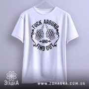 Футболка fuck around find out, білого кольору, підвішена на вішалці, фон світло-сірий, принт з чорними скелетними руками, що показують середній палець, з написом 'AND' та 'FIND OUT'.