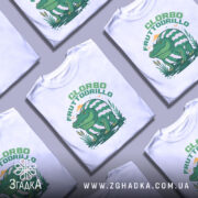 Футболка Glorbo Fruttodrillo білого кольору, зображена з фронтального ракурсу на манекені, фон нейтральний, принт зображає зеленого крокодила, що сидить на воді, з аркушем з водяних лілій і смугастим панцирем.