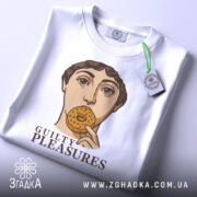 Футболка guilty pleasures, біла, зображена на столі, ракурс зверху, фон світло-сірий, принт з обличчям людини, що тримає печиво, текст 'GUILTY PLEASURES' під принтом, на футболці є бірка.