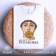 Футболка guilty pleasures, біла, складена на плетеному кошику, фон світло-сірий, принт з обличчям людини, що тримає печиво, текст 'GUILTY PLEASURES' під принтом.