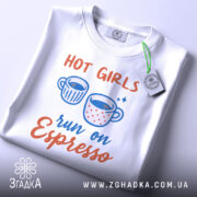 Футболка гарячі дівчата, біла, складена на столі, фон світло-сірий, принт з двома чашками кави та текстом 'run on Espresso', з етикеткою на комірці.