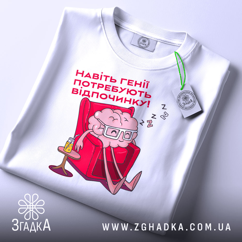 Футболка генії потребують відпочинку, біла, зображена зверху, на фоні світло-сірого кольору, принт з малюнком мозку в окулярах, що сидить у кріслі, текст червоним шрифтом, етикетка з зеленим шнурком.
