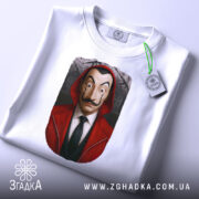 Футболка герой у масці, біла, зображена з верхнього ракурсу, фон світлий, принт з обличчям героя в червоному капюшоні, на футболці є етикетка.