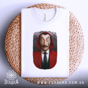 Футболка герой у масці, біла, зображена зверху на плетеній основі, фон світлий, принт з обличчям героя в червоному капюшоні, видно етикетку на горловині.