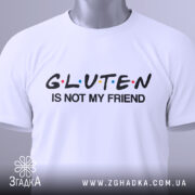 Футболка глютен білого кольору, зображена зверху, на столі, фон світло-сірий, принт чорного кольору з написом 'GLUTEN IS NOT MY FRIEND' та кольоровими крапками, з етикеткою на зеленій стрічці.