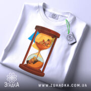 Футболка година війни, біла, зображена на столі, фон світло-сірий, принт з пісочним годинником, на якому одна частина з солдатом, а інша з людиною, що працює на ноутбуці, з етикеткою.