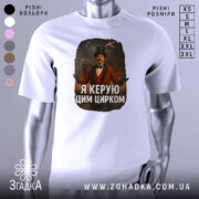 Футболка головний цирк. Біла футболка, зображена з фронтального ракурсу, на манекені. Принт зображає чоловіка в червоному костюмі з капелюхом, який стоїть на фоні циркової арени з акробатами та слоном. Текст на футболці: 'Я керую цим цирком'.