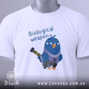 Футболка голуб біологічна зброя, біла, складена на столі, фон світло-сірий, принт з мультяшним птахом у військовому стилі, що тримає зброю, текст 'Biological weapon' над птахом, на етикетці зелений шнурок.