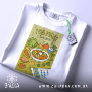 Футболка голубці білого кольору, складена на поверхні, фон світло-сірий, принт з малюнком голубців, овочів та інших страв, прикрашений етикеткою з зеленим шнурком.