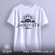 Футболка гори кличуть, білого кольору, підвішена на вішалці, фон світло-сірий, принт чорного кольору з написом 'ГОРИ КЛИЧУТЬ Я МУШУ ЙТИ' та зображенням гір.