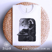 Футболка Горила Діджей білого кольору, складена на плоскій поверхні з плетеного матеріалу, фон світло-сірий, принт з горилою в навушниках, що працює на пульті, з пташками на фоні.