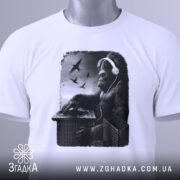 Футболка Горила Діджей білого кольору, складена на плоскій поверхні, фон світло-сірий, принт з горилою в навушниках, що працює на пульті, з пташками на фоні, з етикеткою зеленого кольору.