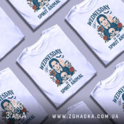 Футболка Готичний Принт, біла, зображена на манекені, фон світло-сірий, принт з зображенням дівчини з косами, яка тримає череп, оточена трояндами та павутиною, текст 'WEDNESDAY IS MY SPIRIT ANIMAL'.