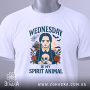 Футболка Готичний Принт, біла, зображена зверху, фон світло-сірий, принт з дівчиною з косами, яка тримає череп, текст 'WEDNESDAY IS MY SPIRIT ANIMAL', на футболці є етикетка з зеленим шнурком.