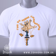 Футболка гра за правилами, біла, складена на поверхні, фон світлий, принт з рукою, що тримає шахову фігуру, з чорними нігтями та жовтим написом, з етикеткою на зеленому шнурку.