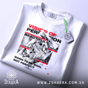 Футболка графічний хаос, біла, складена на плоскій поверхні, фон світло-сірий, принт з текстом у червоному та чорному кольорах, метелики та графічні елементи, на комірці видна етикетка.