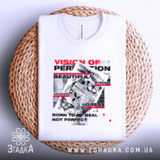 Футболка графічний хаос, біла, складена на плоскій поверхні з плетеного матеріалу, фон світло-сірий, принт містить текст у червоному та чорному кольорах, метелики та графічні елементи.