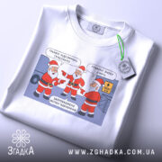 Футболка графіки відключень, білого кольору, зображена на столі з етикеткою, фон світлий, принт з трьома Санта Клаусами, які вказують один на одного, текст на принті українською мовою.