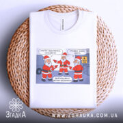 Футболка графіки відключень, білого кольору, складена на плетеній основі, фон нейтральний, принт з трьома Санта Клаусами, які вказують один на одного, текст на принті українською мовою.