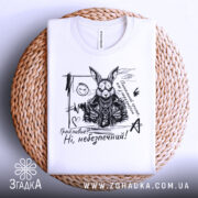 Футболка грайливий небезпечний, білого кольору, зображена зверху на плетеній основі, фон світло-сірий, принт з чорним малюнком зайця в шкіряному жакеті з написом 'Грайливий? Ні, небезпечний!'