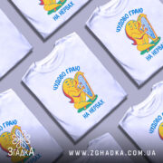 Футболка граю на нервах, біла, зображена на манекені, фон світло-сірий, принт з жовтою фігурою, що грає на арфі, текст українською мовою 'Чудово граю на нервах'.