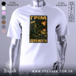 Футболка грім перемоги. Біла футболка з коротким рукавом, зображена на манекені, фон світло-сірий. Принт з військовим персонажем, що стріляє з гармати, на фоні вибухів і українського прапора.