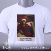 Футболка грінч настрій, складена біла футболка з принтом, на якому грінч у червоному капелюсі та халаті, тримає келих вина, фон - світлий, з легким відблиском, текст під принтом: 'ЩАСЛИВОГО НОВОГО РОКУ'.