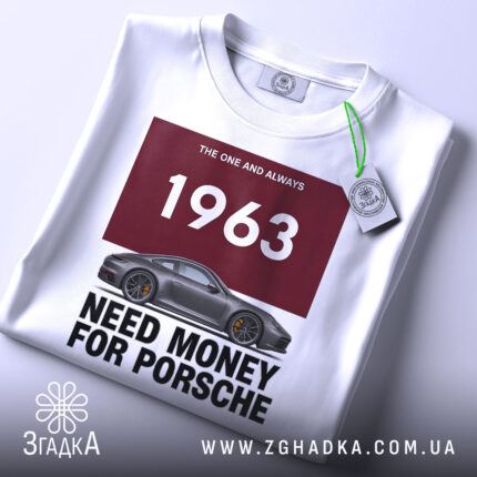 Футболка гроші на машину, біла футболка на столі, ракурс зверху, фон світло-сірий, принт з написом '1963 NEED MONEY FOR PORSCHE' та зображенням автомобіля Porsche, на футболці є етикетка.