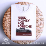 Футболка гроші на Porsche, біла, складена на плетеній тарілці, фон світло-сірий, принт з текстом 'NEED MONEY FOR PORSCHE' червоного кольору та зображенням автомобіля Porsche 718 Cayman GT4 RS.