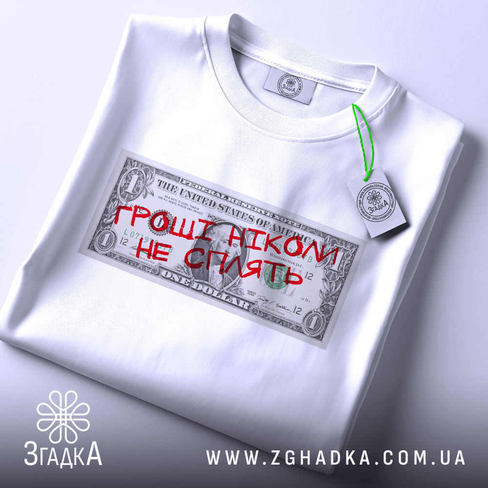 Футболка гроші не сплять, біла, складена на столі, фон світлий, принт у вигляді доларової банкноти з червоним написом "ГРОШІ НІКОМІ НЕ СПІЛЯТЬ", на комірці є етикетка.