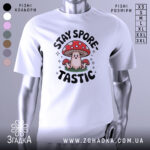 Футболка гриб споретастік білого кольору, зображена з фронтального ракурсу на манекені, фон світлий, принт з веселим грибом та написом 'STAY SPORE-TASTIC' у чорному кольорі з червоними деталями.