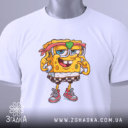 Футболка губка боб білого кольору, складена на столі, з принтом персонажа, на якому видно етикетку з зеленим шнурком, фон білий.