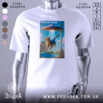 Футболка гумор НЛО, біла, зображена на манекені, фон нейтральний, принт з котом, що летить під космічним кораблем, яскраві кольори, деталі фону включають архітектурні елементи.